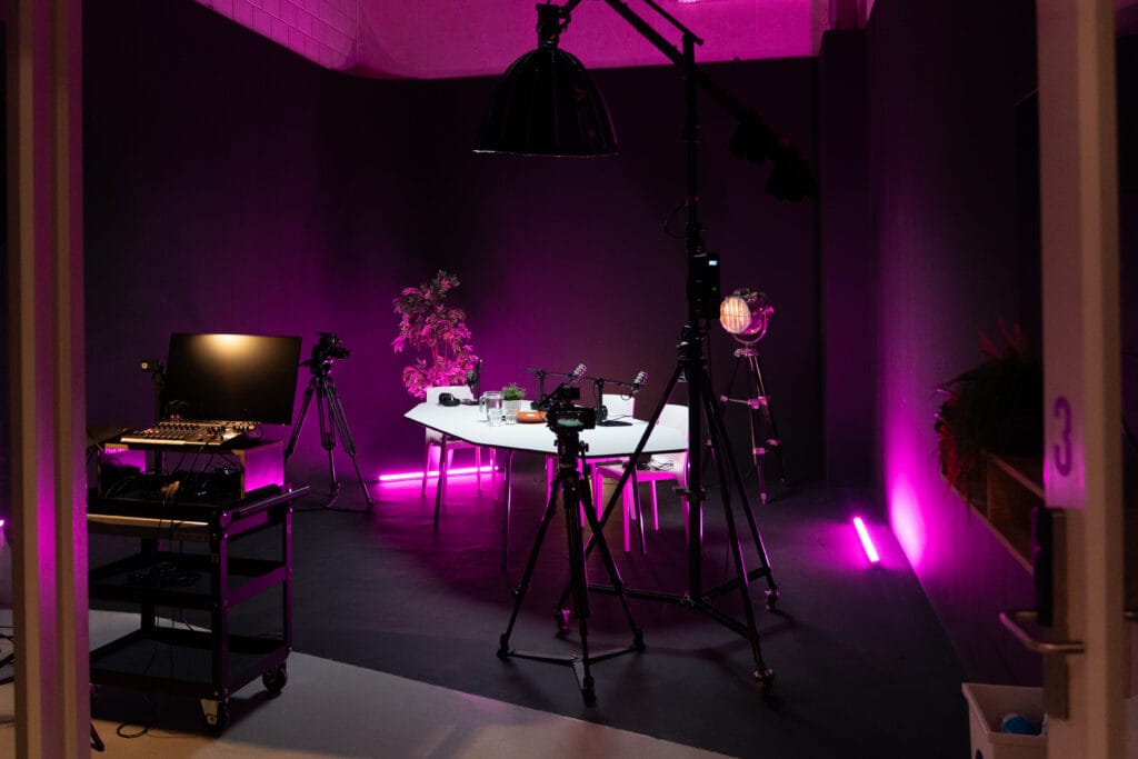 Podcastsetup in donkere ruimte met roze verlichting op de achtergrond.